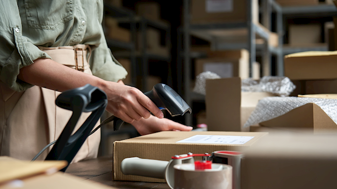 Woman scanning a package in a home-based warehouse, highlighting smart eCommerce logistics and inventory tracking for growing online businesses.