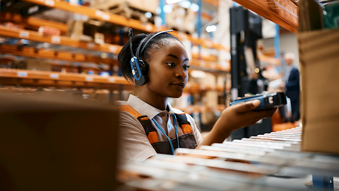 Worker using a handheld scanner with headset in a smart warehouse, emphasizing real-time inventory control in scalable tech logistics operations.